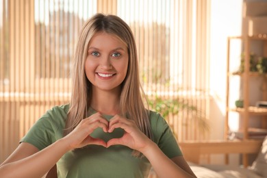 Photo of Happy volunteer making heart with her hands in room. Space for text
