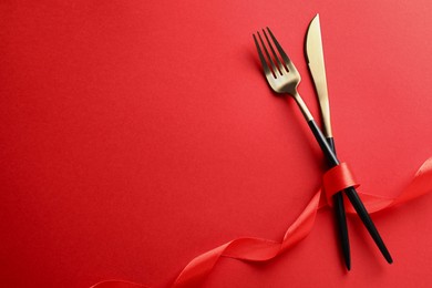 Photo of Cutlery set and ribbon on red background, flat lay with space for text. Romantic table setting