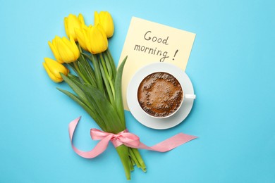Cup of aromatic coffee, beautiful yellow tulips and Good Morning note on light blue background, flat lay