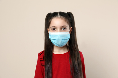 Little girl in medical mask on beige background. Virus protection