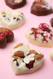 Photo of Tasty chocolate heart shaped candies with nuts on pink background, closeup