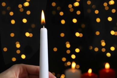 Photo of Woman holding burning candle against blurred Christmas lights, closeup. Space for text