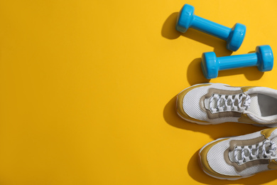 Dumbbells, sneakers and space for text on yellow background, flat lay. Physical fitness