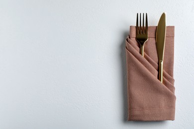 Golden fork and knife with napkin on white table, top view. Space for text