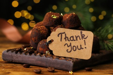 Photo of Chocolate sweets and tag with phrase Thank you on wooden table, closeup