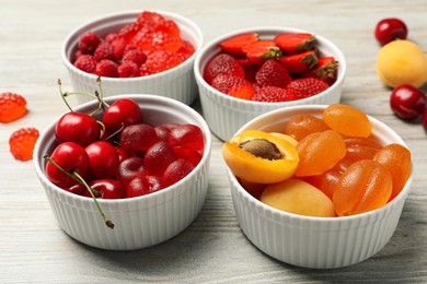 Delicious gummy candies and fresh fruits on white wooden table