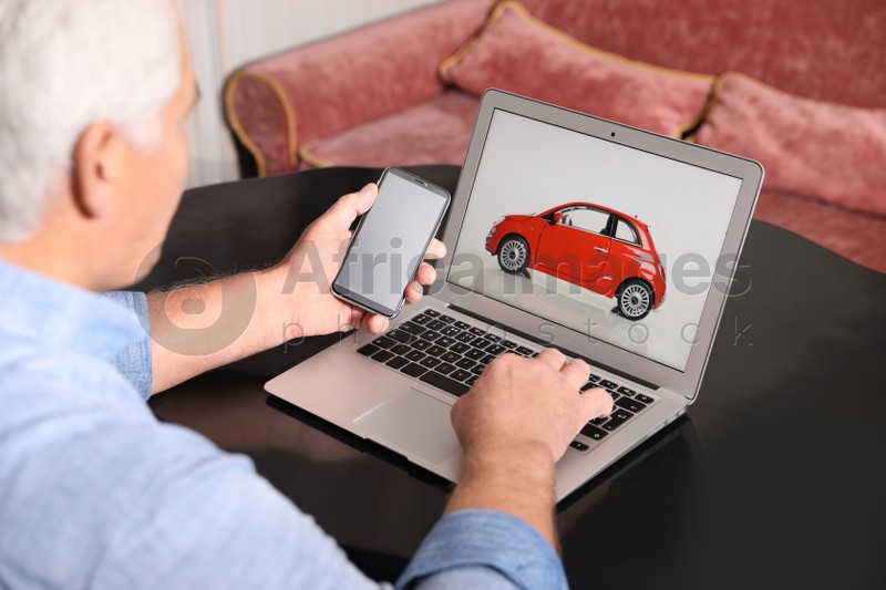 Man using laptop and phone to buy car at table indoors, closeup
