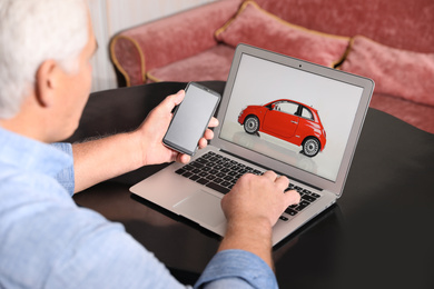 Man using laptop and phone to buy car at table indoors, closeup