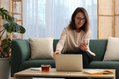 Woman with modern laptop and smartphone learning on sofa at home