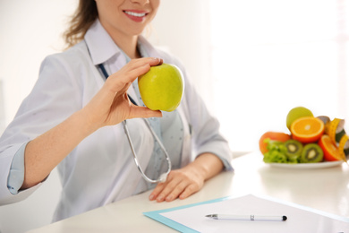 Nutritionist with apple at desk in office, closeup. Space for text