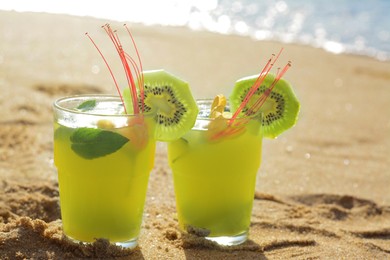 Glasses of refreshing drink with kiwi and mint on sand near sea