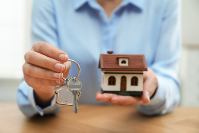 Real estate agent holding house model and key at wooden table, closeup