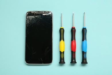 Damaged smartphone and repair tool set on light blue background, flat lay