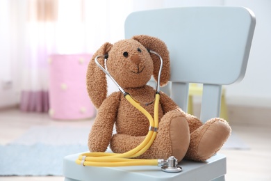 Photo of Toy bunny with stethoscope on chair indoors. Children's doctor