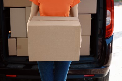 Photo of Courier holding package near delivery truck outdoors, closeup