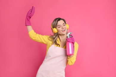Beautiful young woman with headphones and bottle of detergent singing on pink background