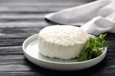 Delicious fresh cottage cheese with parsley on black wooden table, closeup