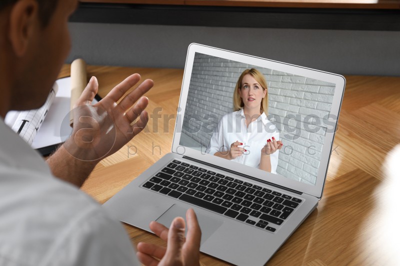 Man talking with beautiful woman using video chat on laptop at wooden table, closeup. Online dating