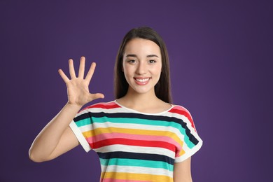 Woman showing number five with her hand on purple background