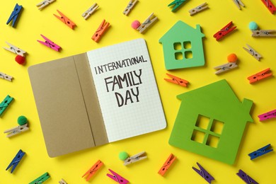 Happy International Family Day. Flat lay composition with notebook and house models on yellow background