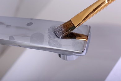 Photo of Using brush and powder to reveal fingerprints on faucet indoors, closeup
