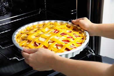 Woman putting raw traditional English apple pie into oven, closeup
