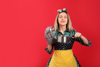 Young housewife with saucepan on red background. Space for text