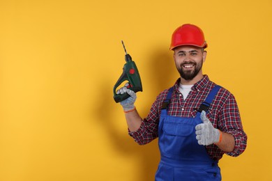 Young worker in uniform with power drill on yellow background. Space for text