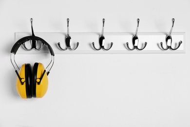 Protective headphones hanging on white wall. Safety equipment