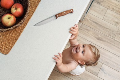 Photo of Laughing little child reaching for knife on light countertop, above view. Dangers in kitchen