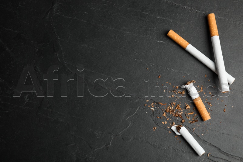 Photo of Broken and whole cigarettes on black table, flat lay with space for text. Quitting smoking concept