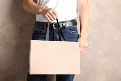 Man holding mock-up of paper shopping bag on color background