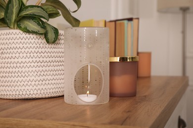Stylish aroma lamp with small candle on wooden cabinet indoors
