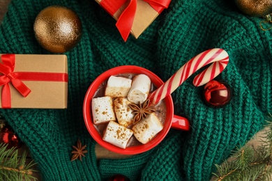 Cup of tasty cocoa with marshmallows, candy cane and Christmas decor on table, flat lay