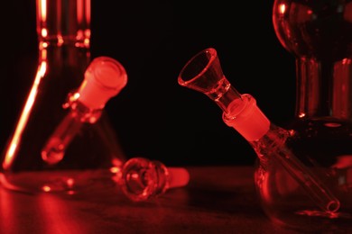 Glass bongs on table against black background, toned in red. Smoking device