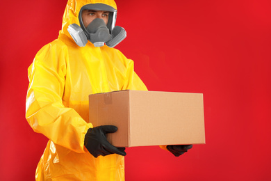Man wearing chemical protective suit with cardboard box on red background. Prevention of virus spread