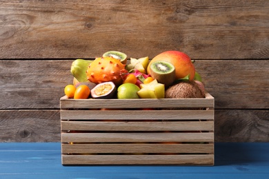 Crate with different exotic fruits on blue wooden table