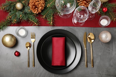 Christmas table setting with plates, cutlery, napkin and festive decor on grey background, flat lay