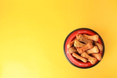 Photo of Bone shaped dog cookies in feeding bowl on yellow background, top view. Space for text