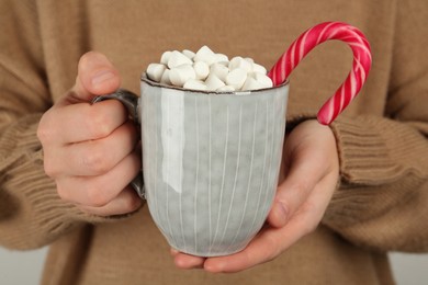 Woman holding cup of delicious hot chocolate with marshmallows and candy cane, closeup