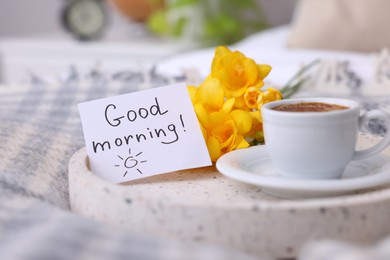 Photo of Cup of coffee, flowers and card with phrase GOOD MORNING! on knitted paid indoors