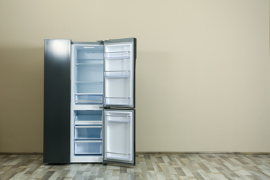 Modern refrigerator near beige wall, space for text