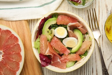 Delicious pomelo salad with prosciutto in half of fruit on white wooden table, flat lay