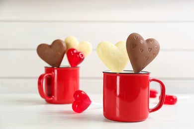 Heart shaped lollipops made of chocolate and sugar syrup on white table, space for text