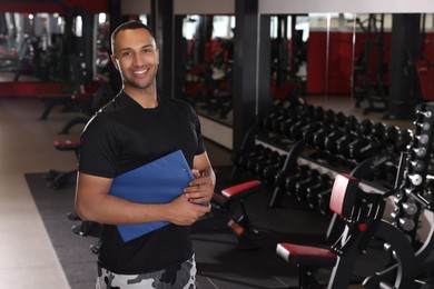 Photo of Happy trainer with workout plan in modern gym, space for text