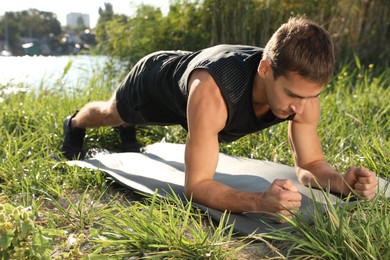 Sporty man doing plank exercise on green grass near river