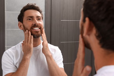 Photo of Smiling bearded man looking at mirror in bathroom