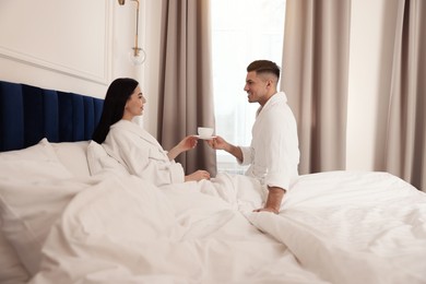 Happy couple wearing bathrobes resting on bed in hotel room