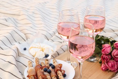 Glasses of delicious rose wine, flowers and food on white picnic blanket