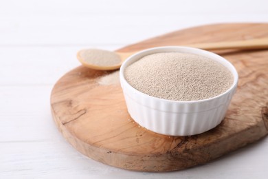 Photo of Bowl and spoon with active dry yeast on white wooden table